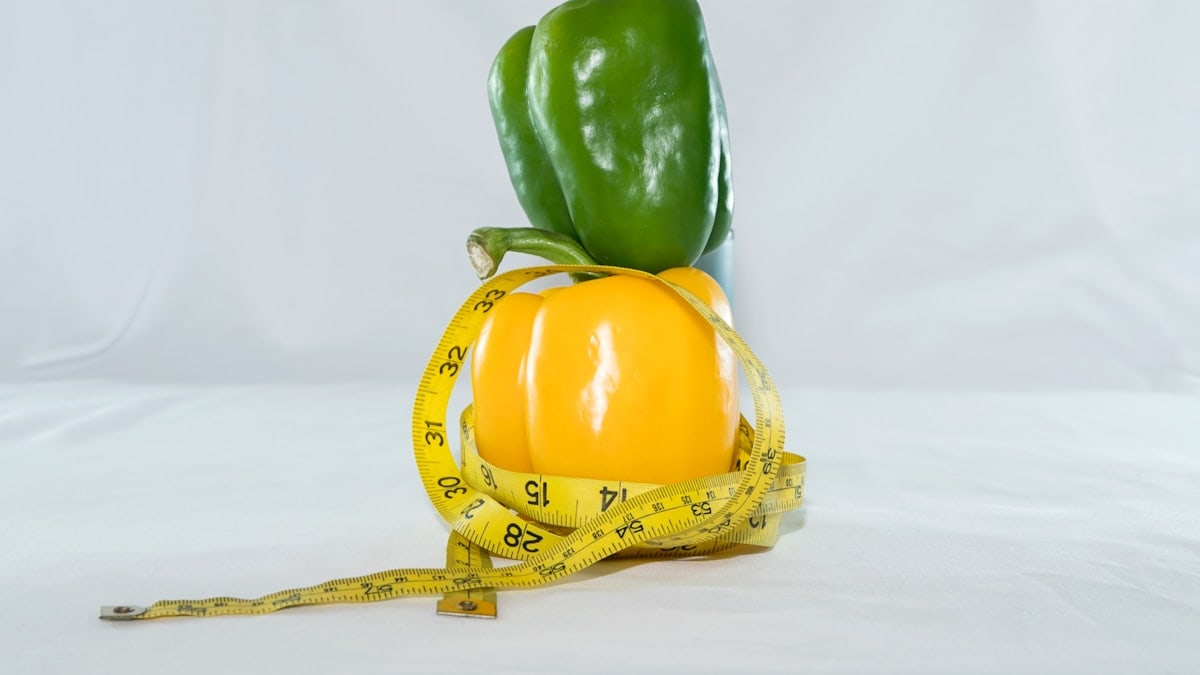 a yellow pepper and a green pepper on a measuring tape